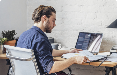 Young man in a dark blue shirt sitting at a table, holding papers, and working from home